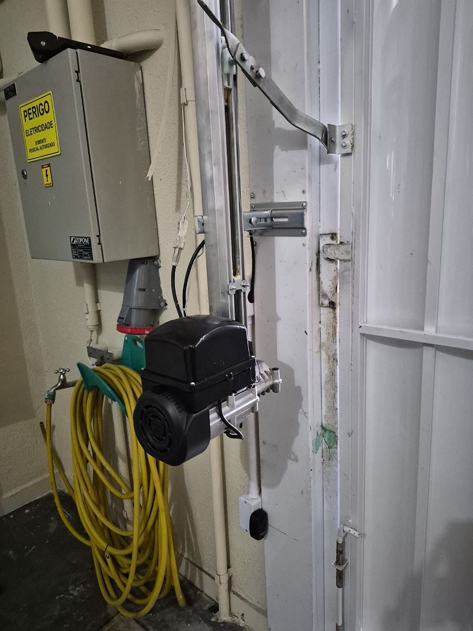 Motor de portão basculante preto instalado na lateral de um portão branco, com o braço e o trilho vertical